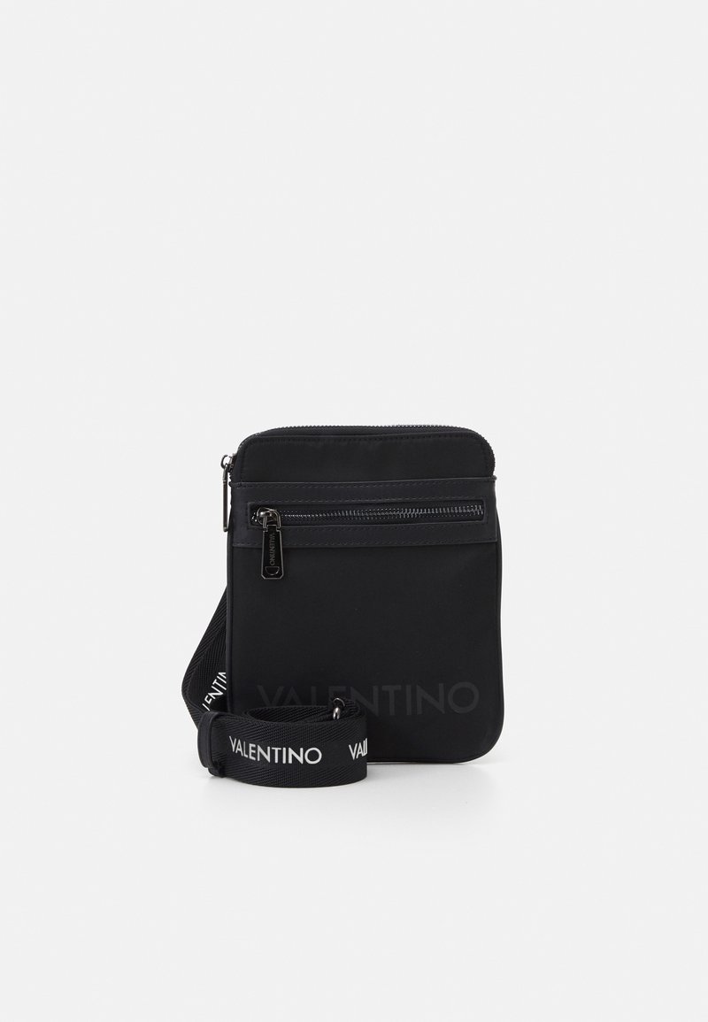 Svart Valentino crossoverväska med framfickor med dragkedja och justerbar axelrem med varumärke, visad mot vit bakgrund.