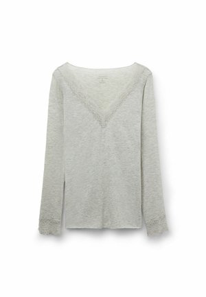 Camisa de manga larga color gris claro con ribete de encaje a lo largo del escote profundo en forma de V y los puños de las mangas, presentada sobre un fondo blanco.