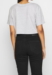 Person som bär en ljusgrå kortärmad topp med cropped design och högmidjade svarta jeans, stående med ryggen vänd framåt.