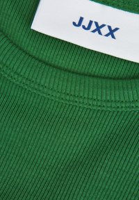 Grüner gerippter Stoff mit strukturierter Oberfläche; verfügt über ein weißes Etikett am Hals mit "JJXX" in Blau gedruckt.