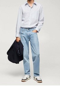 Camisa de botón a rayas azul claro, jeans azules y zapatillas blancas con acentos grises. Blazer negro sostenido con la mano izquierda, de corte relajado.