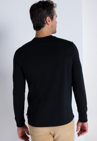 Langärmliges schwarzes Shirt aus weichem Material mit körperbetontem Schnitt, rundem Ausschnitt und ohne sichtbare Muster oder Akzente.