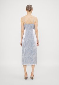Kesdress sepanjang tengah, bertali spaghetti dalam satin biru muda dengan pola floralis halus. Tekstur halus dengan potongan lurus dan belahan samping.