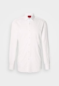 Λευκό βαμβακερό πουκάμισο με μακριά μανίκια, με κλασικό γιακά και εμπρόσθιο κλείσιμο με διάφανα πλαστικά κουμπιά. Ετικέτα ορατή μέσα στον γιακά.