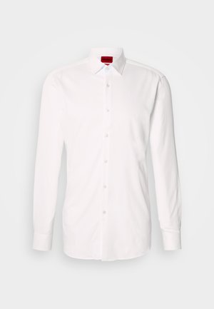 Valge pika varrukaga särk, valmistatud puuvillast, millel on klassikaline krae ja nööbitav esikülg läbipaistvate plastikust nööpidega. Krae sees on nähtav sildi.