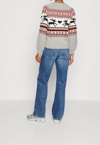 Szary sweter z czarnymi reniferami i czerwonymi geometrycznymi wzorami, zestawiony z niebieskimi spodniami dzwonami. Całość dopełniają srebrne sneakersy.