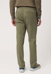 Pantalons vert olive avec une taille élastique, deux poches arrière avec fermetures éclaires, et une coupe droite. Associés à des baskets décontractées.