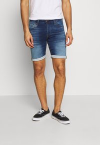 Jeansshorts i blått med en urtvättad gradient, uppvikta ärmar, femfickorsdesign och synliga sömmar. Bärs med svarta sneakers.