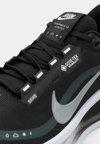 Zwarte Nike hardloopschoen met Gore-Tex Invisible Fit, gedetailleerde veters, branding en weerbestendige iconen op de tong en het zijpaneel.