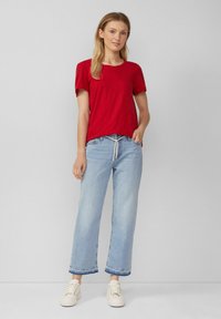 Rode t-shirt met korte mouwen van lichte stof, gecombineerd met lichtblauwe wijde jeans. De schoenen zijn crèmekleurig met een gestructureerd oppervlak.