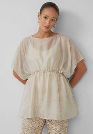 Lichtgewicht, doorschijnend crèmekleurig blouse met een ronde halslijn, vleermuismouwen en een elastische taille. Leggings met kantpatroon eronder.