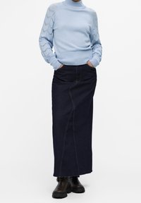 Lichtblauwe gebreide coltrui met textuursleeven, gecombineerd met een lange donkere spijkerrok met zichtbare stitching en zijzakken.