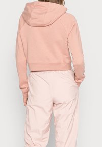 Klippt rosa huvtröja gjord av mjukt tyg, med huva, raglanärmar och en nederkant som sitter strax ovanför midjan.