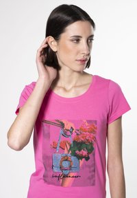 Camiseta rosa con un gráfico colorido de un bolso y flores. El diseño incluye un detallado intrincado y un asa redonda.