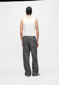 Balti marškinėliai be rankovių ir juodos kelnės su dekoratyviu kraštu. Audinys atrodo minkštas, laisvo silueto, tinkamas kasdieniam dėvėjimui.