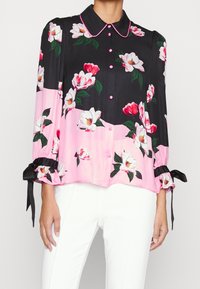 Blusa a bottone floreale con sfondo nero, dettagli rosa, tessuto lucido, colletto e maniche arricciate con legacci in raso nero.