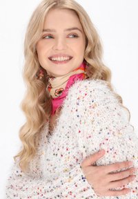 Flauschiger weißer Pullover mit mehrfarbigen Farbtupfern, kombiniert mit einem rosa-beige gemusterten Schal. Weiche Textur und lockere Passform. Langes welliges Haar sichtbar.