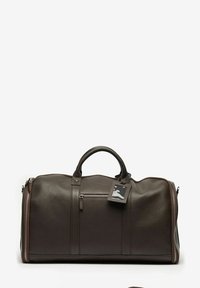 Brun läderresväska med texturerad yta, dubbla handtag och en dragkedjeficka. Utrustad med ett bagagetag fäst vid ena handtaget.