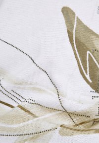 Knitted fabric featuring a white base with beige abstract patterns and decorative metallic beads arranged in flowing lines.