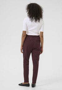 Pantaloni borgogna con vita elastica, aderenti, e tasche posteriori, abbinati a una maglietta bianca a maniche corte. Scarpe nere piatte.