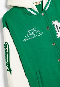 Felpa varsity verde e bianca con chiusura a scatto frontale, testo ricamato e maniche a contrasto con decorazioni.