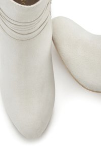 Stivaletti alla caviglia in suede bianco con punta affusolata e dettagli arricciati alla caviglia, caratterizzati da una superficie liscia e una palette di colori neutri.