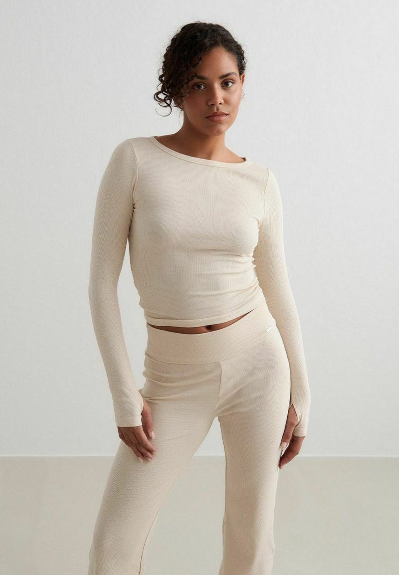 Beige ribbat långärmad topp och matchande högmidjade byxor, mjuk textur, figursydd design, minimalistisk stil, med subtila sömnadsdetaljer.