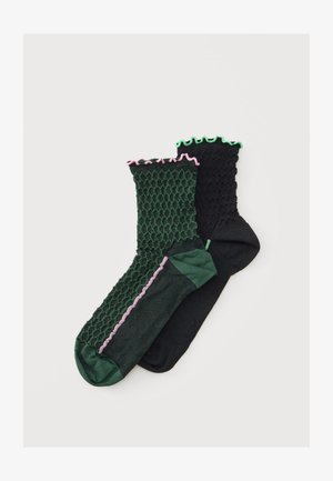 Deux paires de chaussettes basses texturées, une vert foncé avec des bords roses et une noire avec des bords verts, présentées sur un fond blanc.