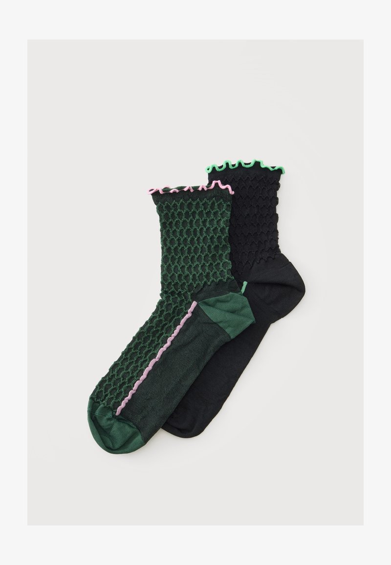 Deux paires de chaussettes basses texturées, une vert foncé avec des bords roses et une noire avec des bords verts, présentées sur un fond blanc.