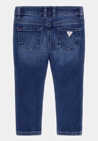 Vaqueros de mezclilla azul oscuro con bolsillos traseros, pasadores para cinturón y un pequeño logo de marca en forma de triángulo en el bolsillo derecho, colocados sobre un fondo blanco.