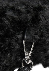 Nahaufnahme einer schwarzen Kunstfelltasche mit einem silbernen Metallverschluss. Auffällige Details sind die strukturierte Oberfläche und die Befestigung des Lederriemens.