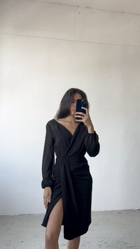 Svart omslagskjole med gjennomsiktige prikker-sleeves, V-hals og høy splitt. Har en knyttet midje detalj og glatt tekstur.