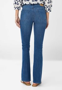 Blauwe uitlopende denim jeans met een medium wasbeurt, voorzien van twee achterzakken en een gestikt tailleband. De stof heeft een zachte textuur.