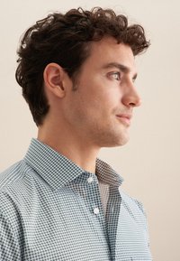 Camicia con bottoni da uomo, caratterizzata da un motivo geometrico blu e bianco, colletto pieghevole e texture liscia. Presenta bottoni bianchi e un design aderente.