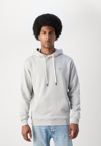 Lichtgrijze hoodie van zacht materiaal met een voorzak, een capuchon met trekkoorden en een klein vierkant logo op de borst. Voorzien van ribgebreide manchetten.