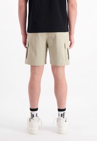 Khaki cargoshorts met zijzakken, gemaakt van lichtgewicht stof. Gedragen met zwarte sokken met witte accenten en witte sneakers.