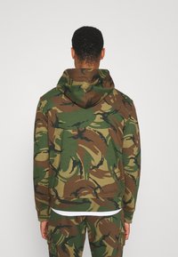 Sudadera con capucha de estampado de camuflaje que presenta tonos verdes, marrones y negros. Confeccionada en tela suave, con mangas largas y un corte relajado.