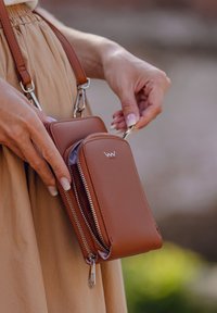 Brown leather crossbody bag with a smooth texture, two zippered compartments, and silver hardware. Adjustable strap for versatile use.