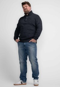Donkergrijze gebreide trui met een hoge kraag en twee knopen, gecombineerd met blauwe jeans en witte sneakers met zwarte strepen.
