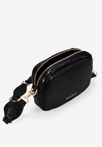 Bolso de cuero negro con acabado texturizado, cremalleras dobles, herrajes dorados y una correa ajustable con acentos redondeados. Logo de la marca visible.