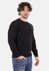 Maglione nero realizzato in un materiale a maglia testurizzato, con maniche lunghe e scollatura rotonda. Include un piccolo logo sul petto.