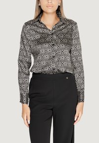 Blusa a motivi bianco e nero con colletto, chiusura a bottoni, maniche lunghe e texture liscia e setosa.