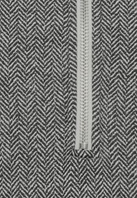 Tissu à motif chevrons noir et blanc avec une fermeture éclair argentée verticale, présentant un design structuré et texturé.