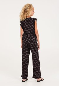 Zwarte, gestreepte jumpsuit met gerimpelde mouwen en wijde broekspijpen; benadrukt een roze bloemenontwerp tegen een effen achtergrond; gladde stoftextuur.