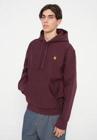 Bordo dukserica s kapuljačom, napravljena od mekanog pamuka, sa prednjim džepom i malim žutim logom na prsima. Opusti fit s rebrastim manžetama.