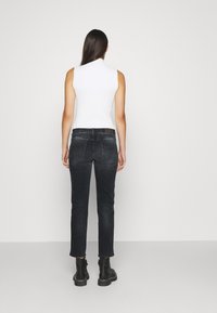 Top bianco a coste senza maniche abbinato a jeans grigi scuri aderenti, con vita standard e piccole tasche posteriori; indossato con stivali neri alla caviglia.