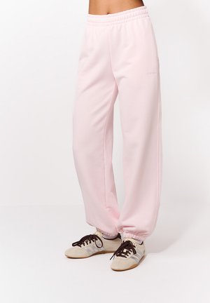 Jasnoróżowe spodnie dresowe wykonane z miękkiego materiału, z elastycznym pasem i marszczonymi mankietami. W połączeniu z beżowo-szarymi sneakersami.