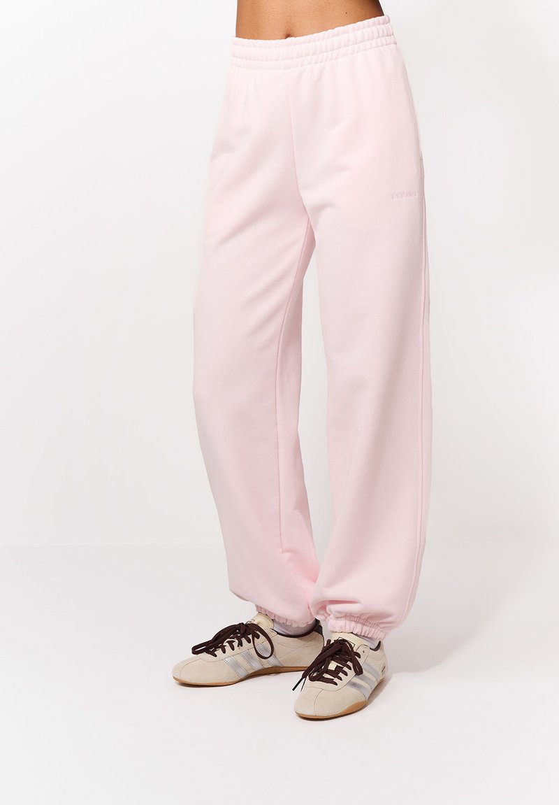 Svetloružové tepláky z mäkkej látky s elastickým pásom a naťahovacími manžetami. Skombinované s béžovými a sivými teniskami.