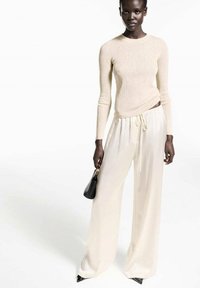 Maglione beige a costine a maniche lunghe abbinato a pantaloni larghi crema; l'outfit presenta una vita con coulisse e una borsa nera.