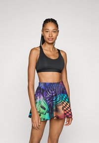 Soutien-gorge de sport noir et jupe courte multicolore présentant un design graphique avec des motifs à carreaux, des dégradés vibrants et une taille élastique.